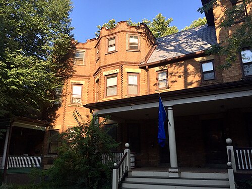 Red brick rowhouses on Hessler Road with front porches and bay windows, framed by green trees.
