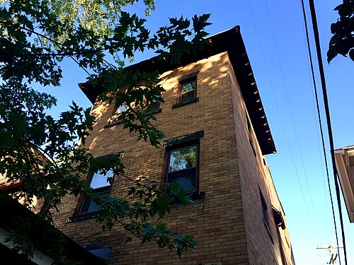 A three storey yellow brick residential building on Hessler Road seen from a low angle, tree leaves and power lines against the sky.