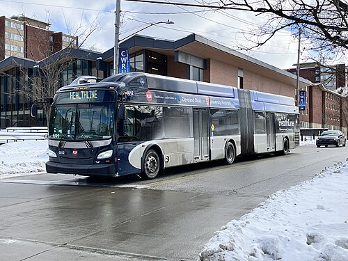 An articulated blue and silver HealthLine bus on Euclid Avenue, snow at the roadside, brick university buildings behind it.
