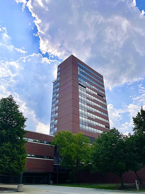 A tall red brick modern building framed by trees under a blue sky.