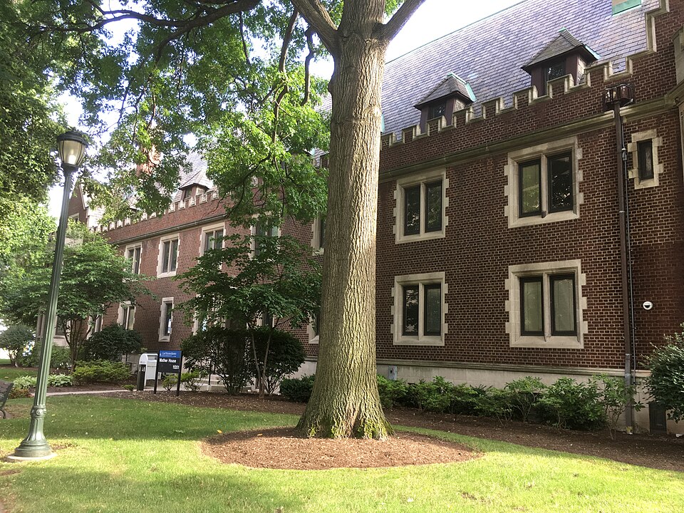 Mather House, a three storey dark red brick Gothic building with stone trim, crenellations and dormers, behind a large tree and open lawn on Adelbert Road.