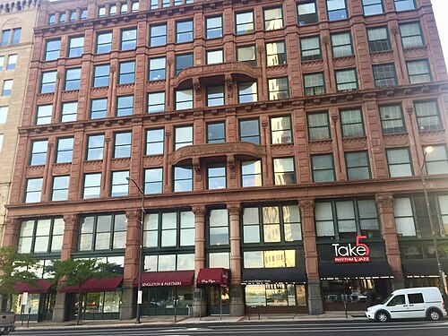 The Perry-Payne Building's rusticated brownstone front, eight storeys of arched window bays over ground floor law office and jazz club storefronts.