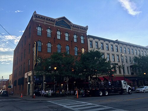 The corner of West 6th Street, red brick building painted with L.F. and S. Burgess Grocers lettering, a cream stone building beside it, a delivery truck at the curb.