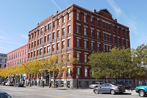 The Grand Arcade, red brick with cream stone trim and its name carved into the cornice, ground floor shops along a tree lined corner.