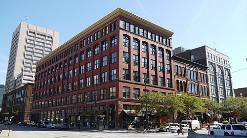 A six storey red brick warehouse building at a wide downtown intersection, a modern glass tower and an older stone building alongside it.