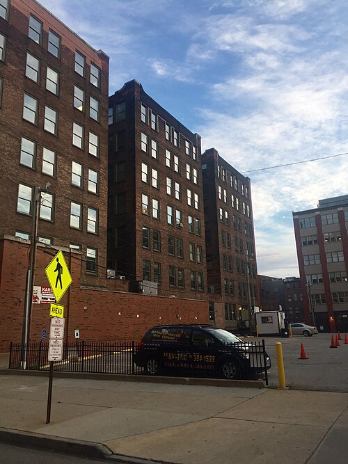The dark brick rear elevations of two warehouse buildings facing a surface parking lot, a pedestrian crossing sign at the edge of the lot.