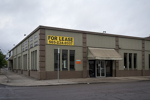 A single storey concrete block warehouse on a corner, built in 1928, with a canvas awning over its entrance.