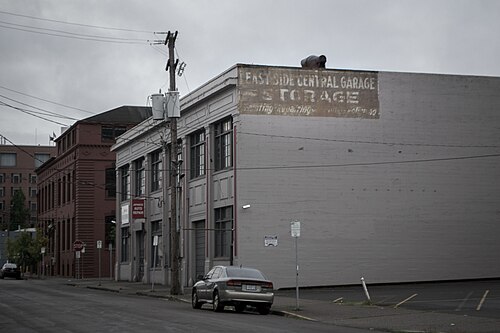 A faded painted sign reading EAST SIDE CENTRAL GARAGE STORAGE on the blank brick side wall of a warehouse, an auto repair shop next door.