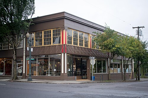 A two storey rounded corner building with red and cream trim, striped awnings over the ground floor storefront.