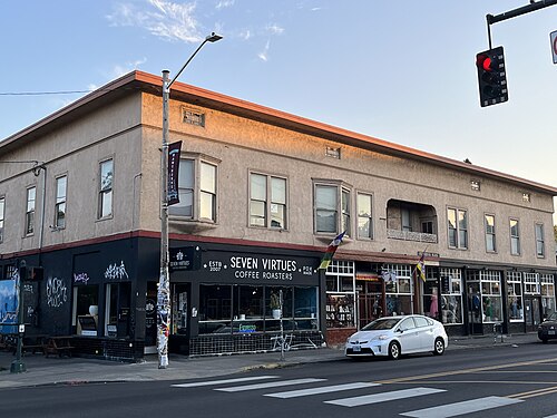 A black storefront under a two storey stucco building on the corner, with a Hawthorne banner hanging from the streetlight.