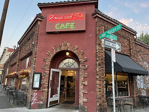 The Bread and Ink Cafe's brick corner at 36th Avenue, a tiled roof and arched brick entrance, cafe tables set out behind a bike rail.