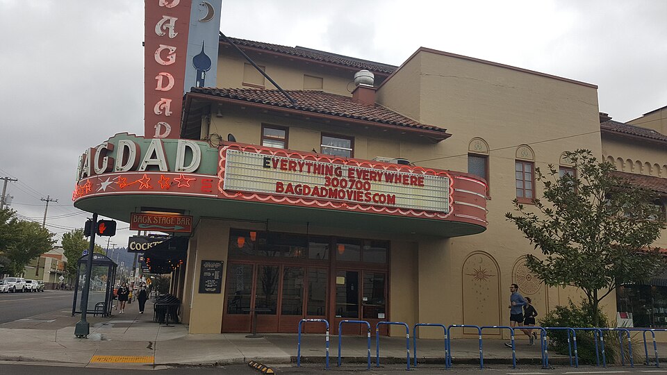 The Bagdad Theatre's corner marquee reading BAGDAD, the Back Stage Bar sign below it, and the stucco front along the sidewalk with runners passing the bike railing.