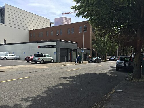 A low grey block building beside a taller brown brick warehouse on NW 9th Avenue, a construction crane visible over the rooftops. Photographed in 2016, when the storefront carried Blackfish Gallery's sign; the gallery relocated to NW Everett Street in 2021.