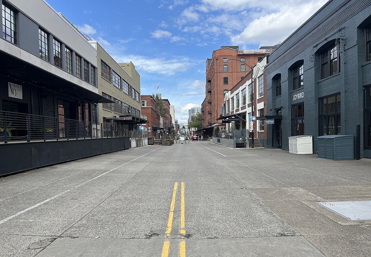 NW 13th Avenue's brick and painted masonry warehouse blocks, awnings over ground floor shops, a double yellow line running down the center of a nearly car free street.