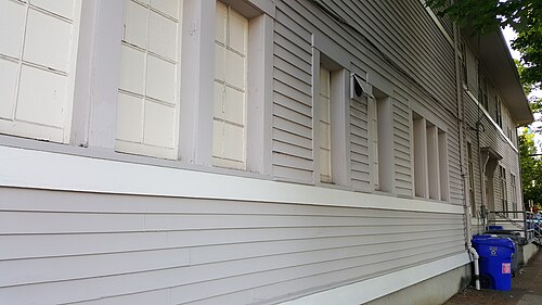 A side wall of the Sellwood Community Center, wood clapboard siding with paired double-hung windows in white surrounds.