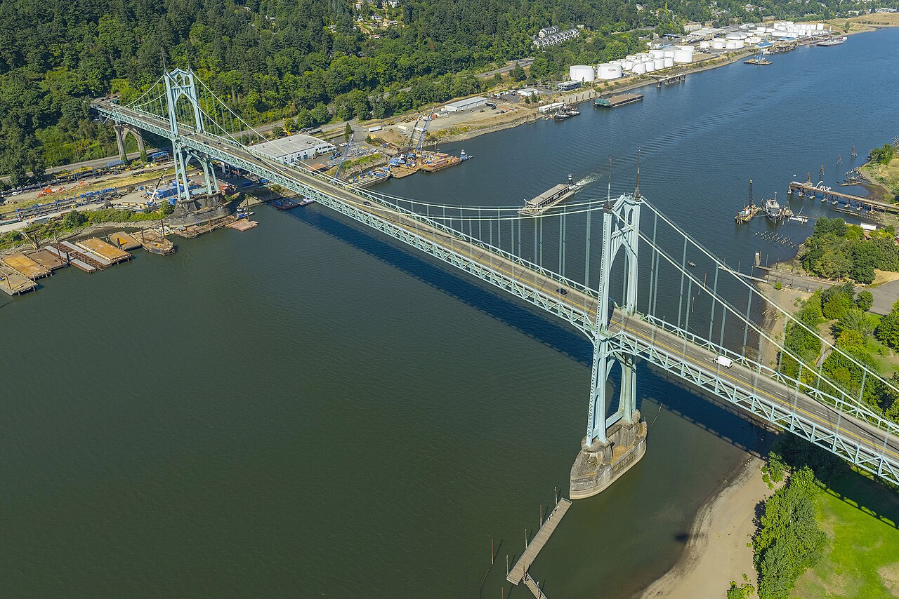 An aerial view of the bridge's north bank, rows of oil storage tanks and barges moored along the industrial riverfront.