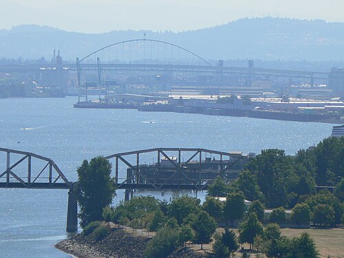 The view south from the bridge deck, a steel rail bridge and dock cranes along the river's industrial edge.