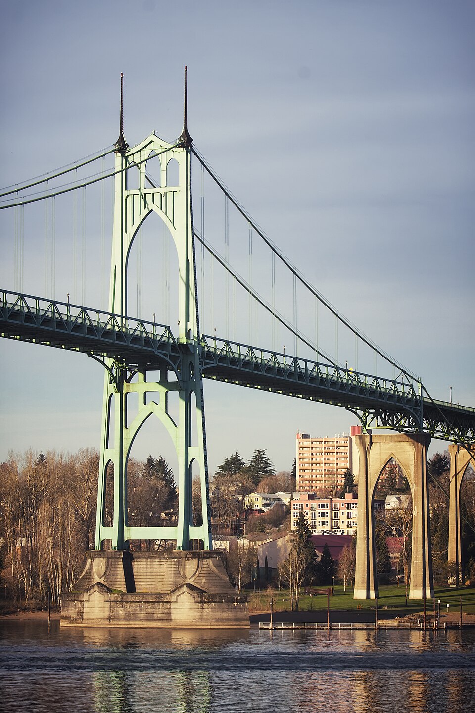 The bridge's east tower and roadway trusses, painted green, seen from the southwest with the riverbank park below.