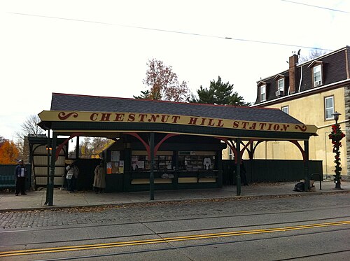 A wooden trolley station shelter lettered Chestnut Hill Station, cobblestone street with trolley rails out front.