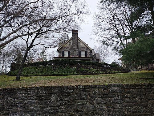 A grey stone mansion on a rise above a low fieldstone wall, a gabled roofline with a central chimney.