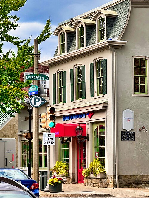 A stucco building with a mansard roof and three arched dormers, green shutters and a red canopy over the door.