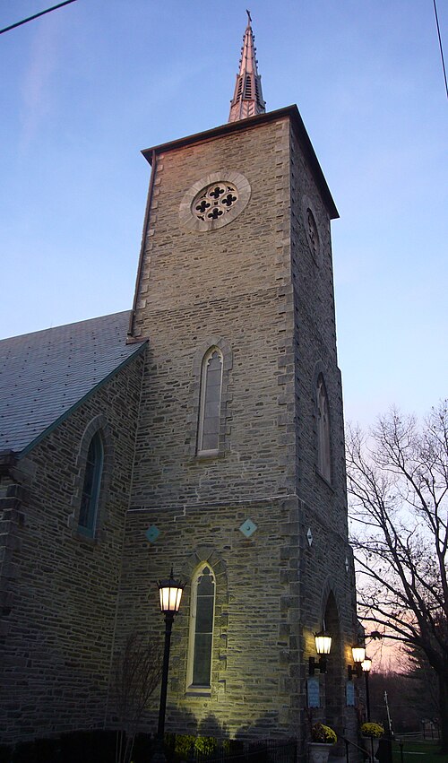 A grey stone church tower with a rose window and a copper spire against the evening sky.
