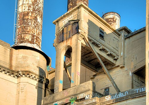 A concrete tower with an arched base and two rusted smokestacks at the former PECO Delaware Generating Station, graffiti tags along its lower walls.