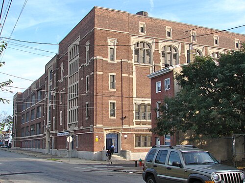A four storey brick and stone school building wrapping a street corner, arched upper windows and a columned entrance porch.