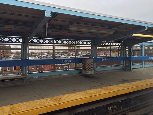 The elevated Berks platform under its canopy, rowhouse rooftops visible beyond the trackside mesh screen.