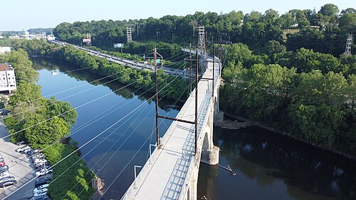 An aerial view of the Manayunk Bridge's concrete arches carrying the trail high over the Schuylkill River and the tree line.
