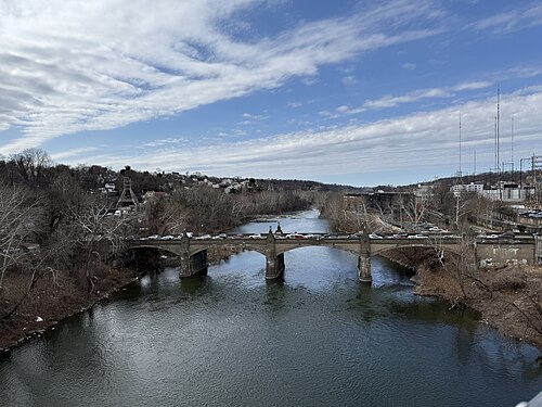 A stone piered road bridge crossing the river, cars on the deck and hillside houses and radio towers in the distance.