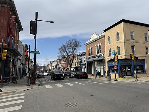 Main Street at Cotton Street, storefronts and a corner building under traffic signals, cars parked along both curbs.