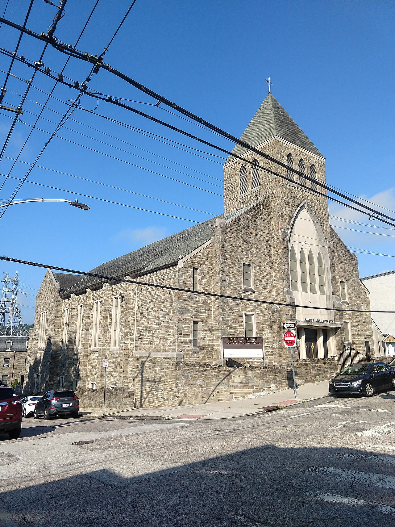 Saint Josaphat's stone church and spire at a sloped street corner, power lines crossing overhead.