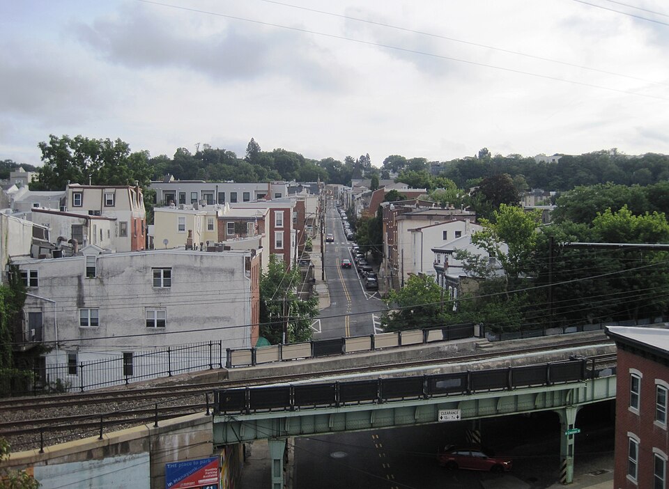 Green Lane climbing steeply away from Cresson Street, rowhouses packed along both sides and a rail trestle crossing in the foreground.