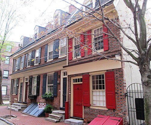 Two red brick rowhouses on Cuthbert Street, one with black shutters and dormer windows, a For Sale by Owner sign on the stoop.