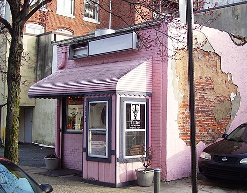 A single storey pink painted storefront at 212 Arch Street, a bakery sign in the window and a patch of exposed brick showing through the stucco next door.