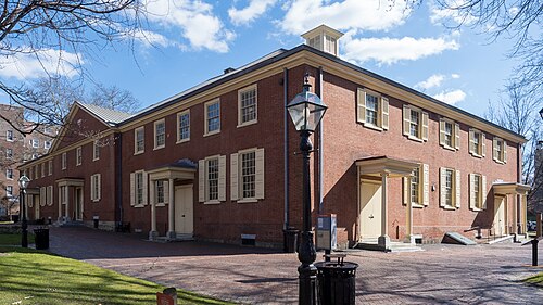 The Arch Street Friends Meetinghouse, a long two storey red brick hall with shuttered windows, a cupola and a brick paved yard.