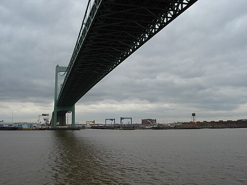 The Benjamin Franklin Bridge's green steel span crossing the Delaware, cranes and a water tower on the working shoreline below.