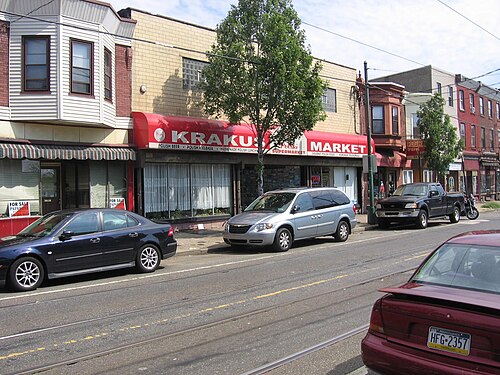 Brick rowhouses and shopfronts on Richmond Street, a red awning over one storefront, SEPTA trolley tracks set into the road and parked cars along the curb.