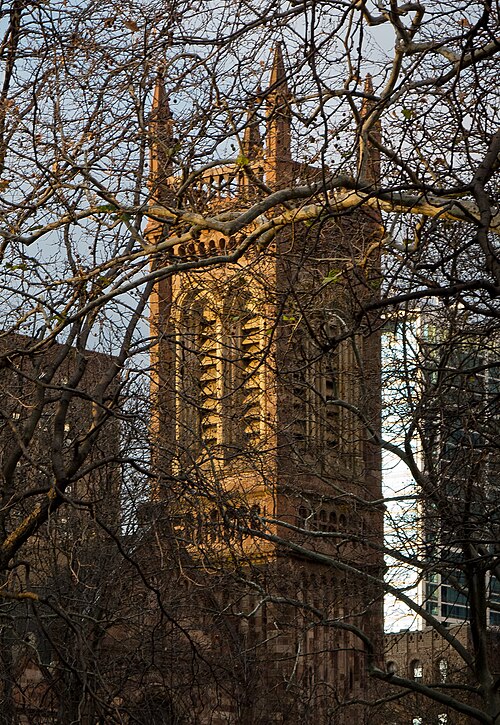 A brownstone church tower framed by bare tree branches.