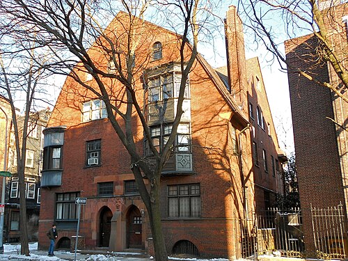 A four storey red brick double house with arched entry doorways, oriel bay windows and steep gambrel gables.