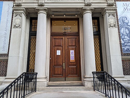 A monumental stone entrance portico with paired columns flanking double wooden doors and black iron railings.