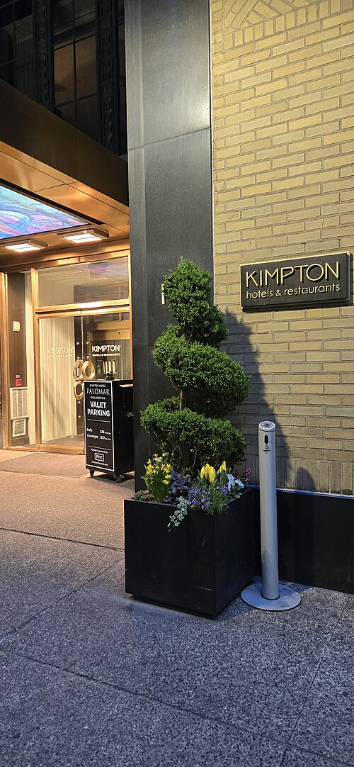 The Art Deco hotel entrance at night, a glass door with brass trim, a spiral topiary and wall signage.