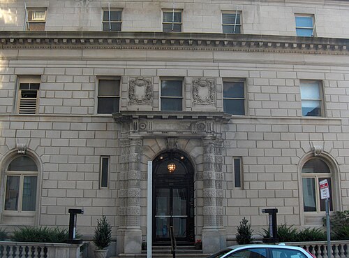 A symmetrical limestone mansion facade with classical arched openings, carved stone trim and potted plants by the door.
