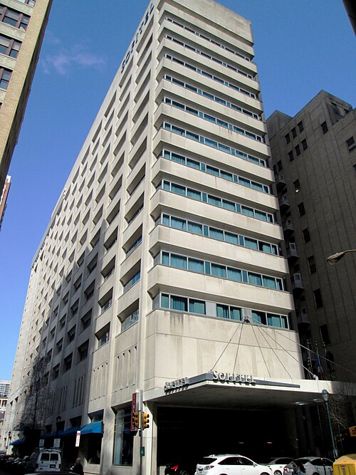 A hotel entrance canopy and glass doors at street level, looking up at the tower above.