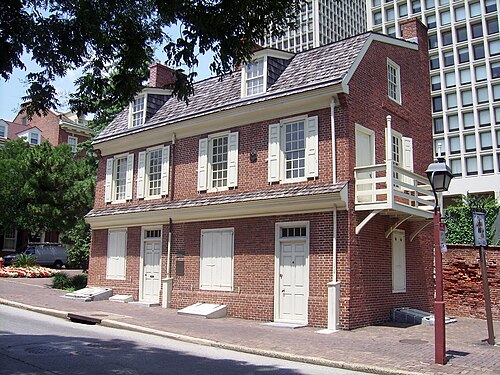 The Man Full of Trouble Tavern on Spruce Street, a two storey red brick building with white shuttered windows, a wood shingle roof and a small side balcony over the door.