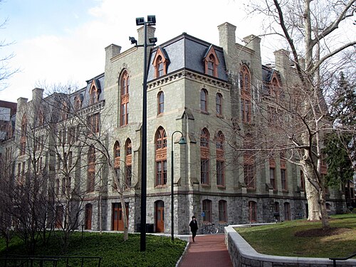 Claudia Cohen Hall in pale stone, pointed arched windows and dormers under a slate mansard roof, a single figure on the path below.