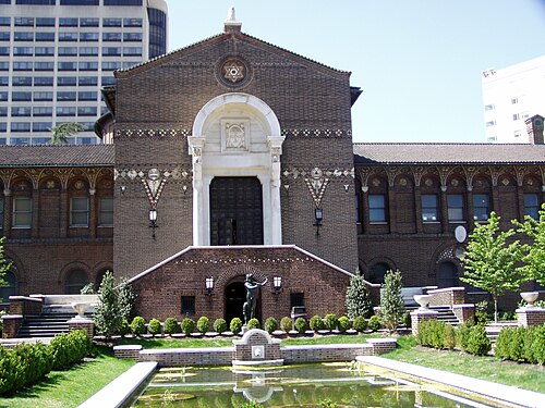 The Penn Museum's brick and terracotta entrance front, a reflecting pool and a bronze fountain figure in the foreground.