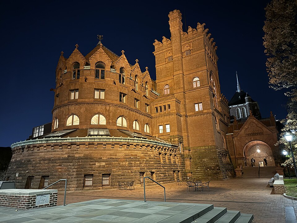 Fisher Fine Arts Library at night, red sandstone round towers over a paved plaza and a lit stone stair.