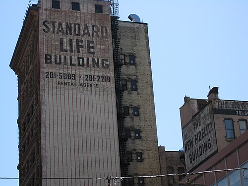 Painted ghost signs reading Standard Life Building and The New Fidelity Building high on the brick sides of two downtown office towers.